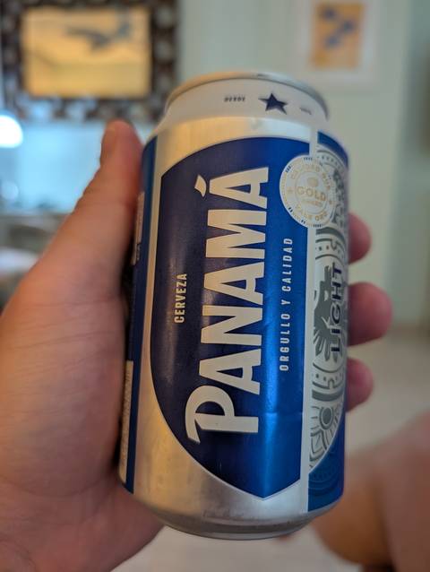 Hand holding a chilled blue can of Panamá beer in soft indoor light.