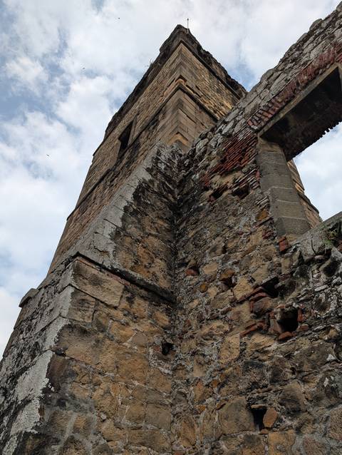 Upward perspective of an aged stone tower wall with weathered bricks against a cloudy sky.