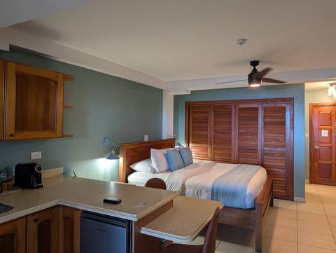 Cozy studio room with double bed, kitchenette, and ceiling fan lit by warm lamps.