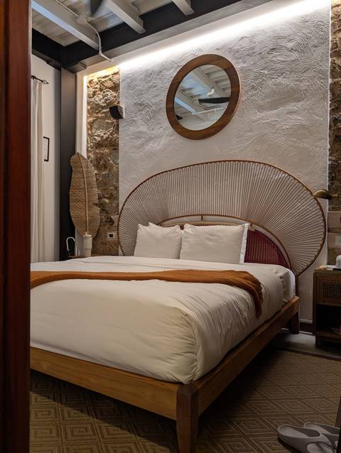 Stylish hotel room with rattan headboard, crisp white bedding and warm accent throw.