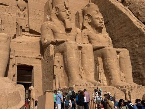 Visitors stand beneath the colossal seated statues of Abu Simbel carved into sandstone cliffs.