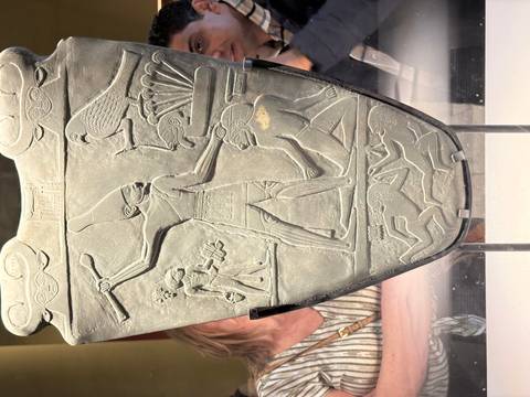 Close-up of the ancient Narmer Palette displayed in a museum glass case with visitors behind.