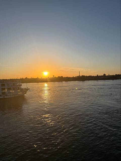 Orange sunset reflecting on the Nile River with cruise boat and palm silhouette.