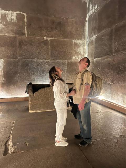 Couple inside granite chamber of an ancient pyramid looking up at towering walls.