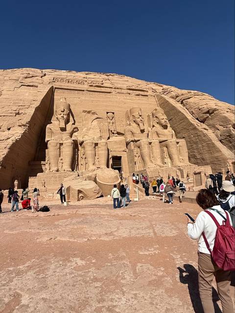 Monumental façade of Abu Simbel with seated pharaoh statues and tourists milling around.