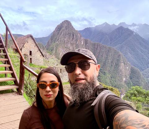 Couple selfie in front of Machu Picchu terraces and Huayna Picchu peak.