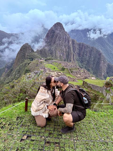 Couple sharing a kiss with Machu Picchu ruins sprawling below them.