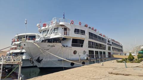 Large white Nile cruise ship docked at a riverside pier on a sunny day.