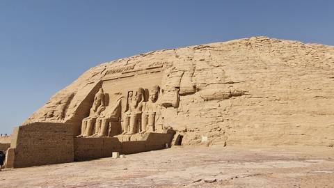 Colossal rock-cut façade of Abu Simbel with four seated statues carved into a sandstone cliff under a clear sky.
