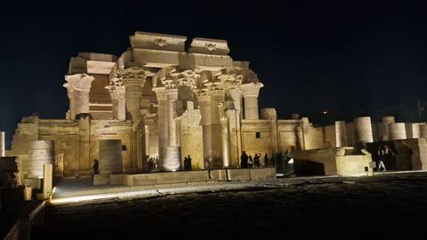 Kom Ombo Temple illuminated dramatically at night with visitors silhouetted against ancient columns.