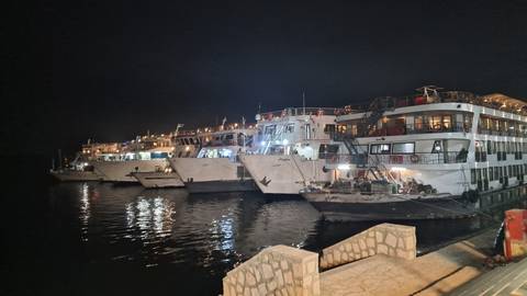 Row of brightly lit Nile cruise ships moored side by side on calm night waters.