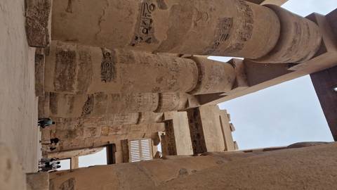 View up towering hieroglyph-covered columns inside Karnak Temple with visitors exploring the ancient site.