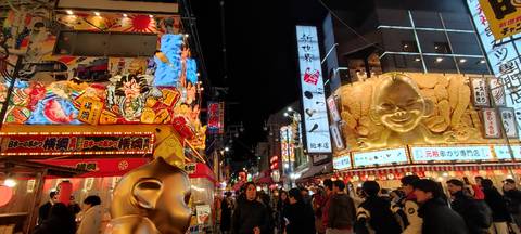Bustling night market street lined with bright neon signs and colorful billboards in Osaka.