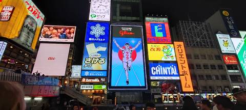 Famous Glico running man sign among many illuminated billboards in busy Dotonbori at night.