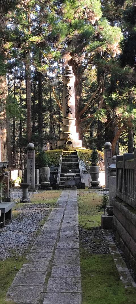 Moss-covered stone stupas and grave markers in a shaded forest cemetery.