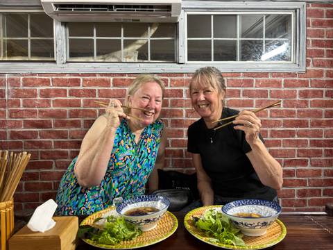 Two women smiling with chopsticks ready to eat Vietnamese food