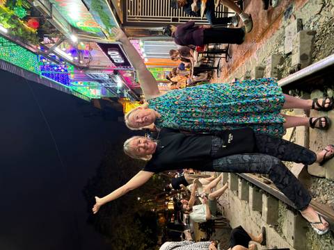 Energetic night-time pose of two women on train tracks lined with cafés and lights