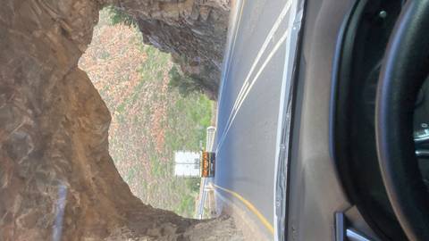 View through a car windscreen driving through a narrow rock tunnel behind a truck on a winding road.