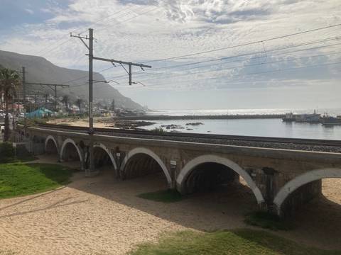 Coastal railway viaduct with multiple arches beside sparkling sea and a mountain backdrop.