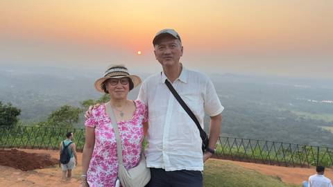 A couple posing in front of a hazy sunset panorama from a hilltop viewpoint.