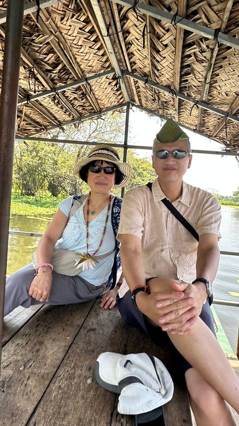 Two travellers seated on a small open boat cruising through a lily-covered lagoon.