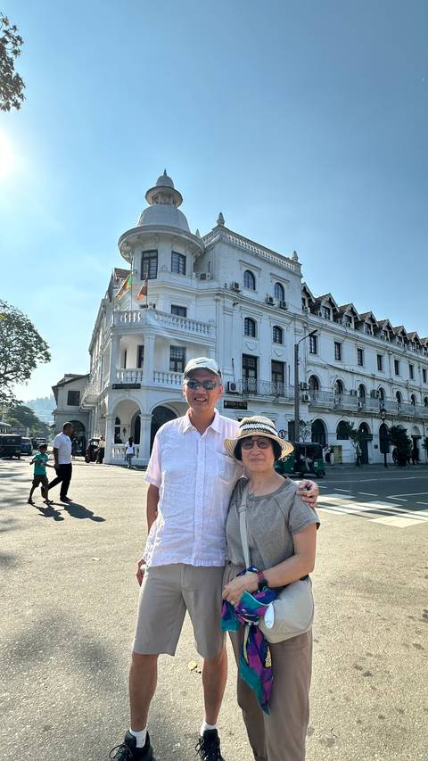 A couple posing in front of a grand colonial-era white building on a sunny city street.