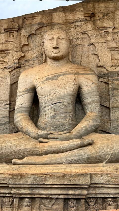Detail of a seated stone Buddha statue with intricate carvings on the torso and surrounding rock.