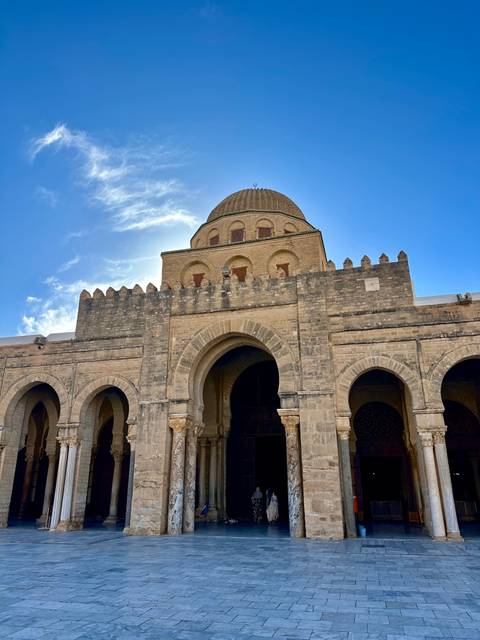Grand entrance of the Great Mosque with arched doorways and crenellated walls against blue sky.