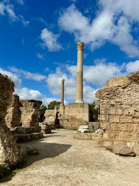 Ruins of ancient stone columns and walls under a bright blue sky in Carthage.
