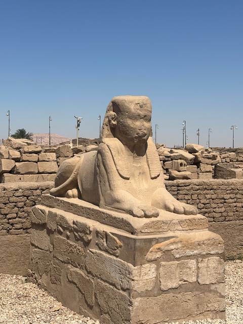 Stone sphinx statue in an open-air section of Karnak Temple against a blue sky