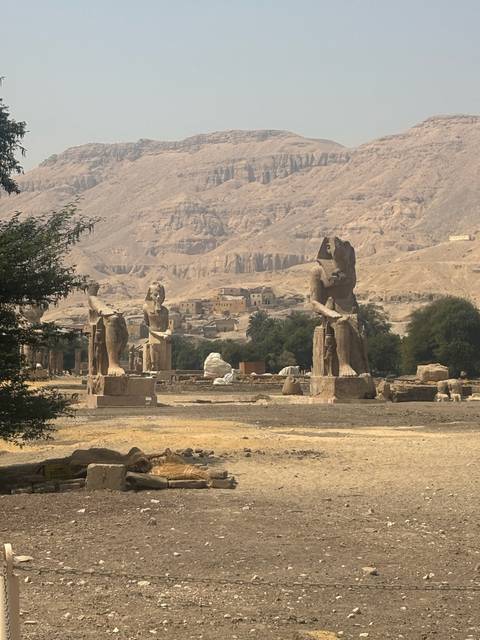 Colossi of Memnon statues standing in a desert landscape with rugged hills behind