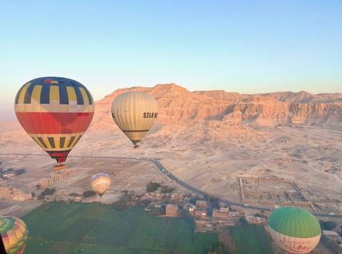 Colorful hot air balloons float above the desert cliffs and green fields of Luxor at sunrise