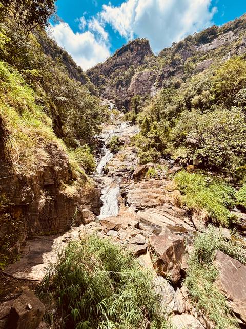 Tall multi-tiered waterfall cascading over rocky cliffs surrounded by lush green forest