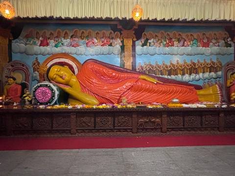Colorful reclining Buddha statue inside an ornately painted temple hall with flower offerings