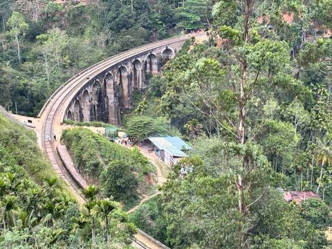 Historic Nine-Arch railway bridge curving through dense green jungle seen from above