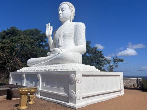Large white seated Buddha statue on a pedestal against bright blue sky