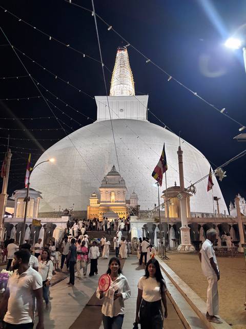 Massive white stupa illuminated at night with crowds of worshippers in white garments