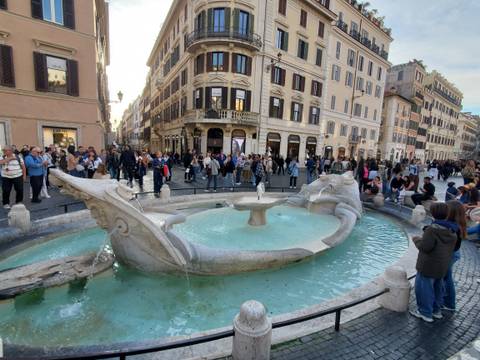 Crowds surround the Barcaccia Fountain at the foot of Rome's Spanish Steps on a sunny afternoon.