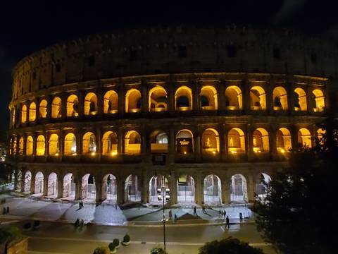 The Colosseum glows with golden illumination against the night sky, its ancient arches in sharp relief.