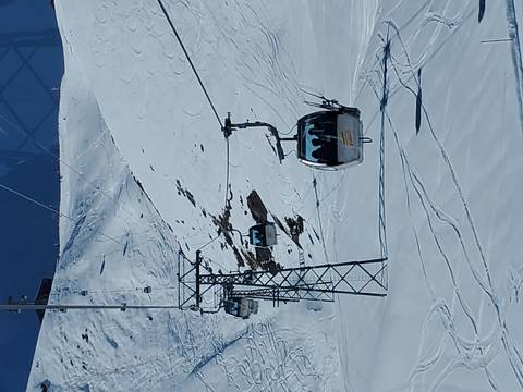 Enclosed ski gondolas glide above fresh powder snow on a high alpine slope.