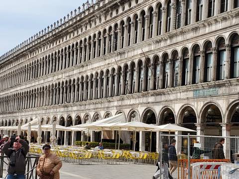 The elegant arched façade of Venice's Procuratie lines St. Mark's Square with outdoor café tables below.