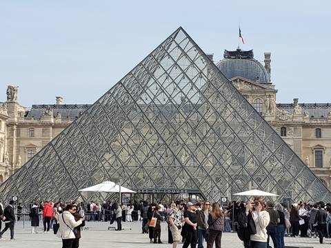 Crowds gather outside the Louvre Glass Pyramid on a clear day in Paris.