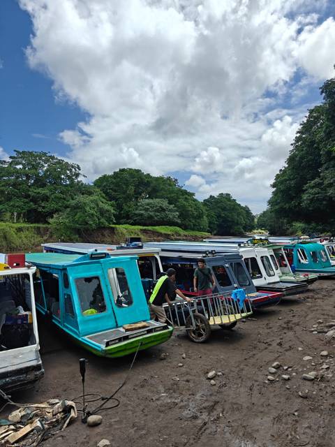 Row of colorful river boats with travelers boarding amid tropical forest surroundings
