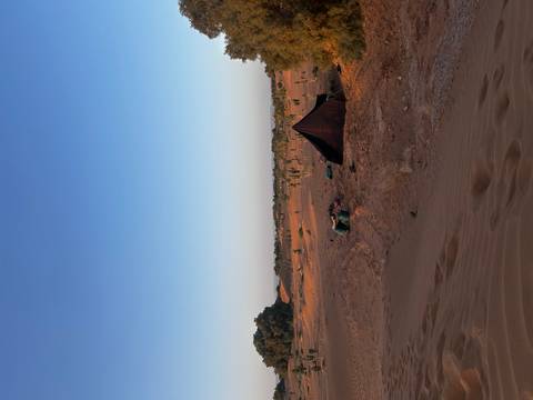 Simple Berber tent and supplies rest on an open sandy plain under a clear dawn sky.