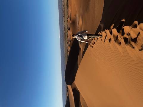 Traveler walks the crest of tall orange dunes leaving a trail of footprints in Morocco’s Sahara.