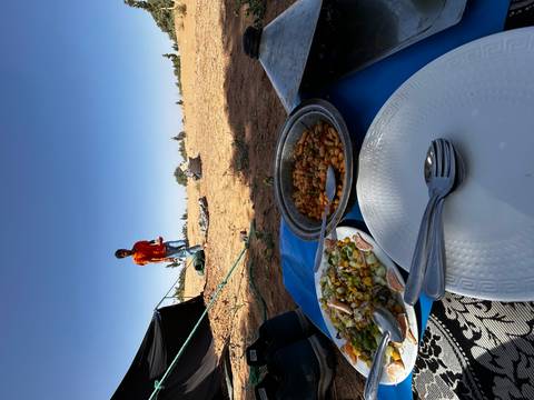 Desert picnic of bean tagine and salad set on a low table while guide works in background.