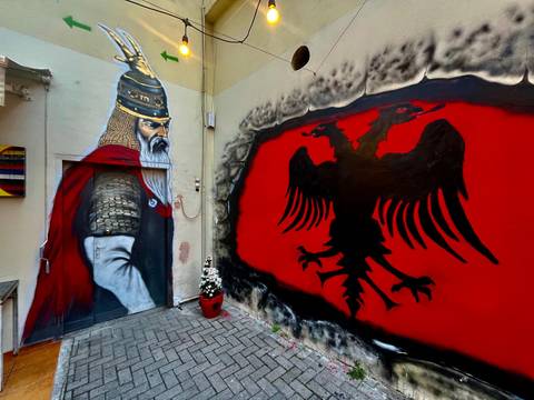 Street art mural depicting historical Albanian figure and red double-headed eagle flag emblem.