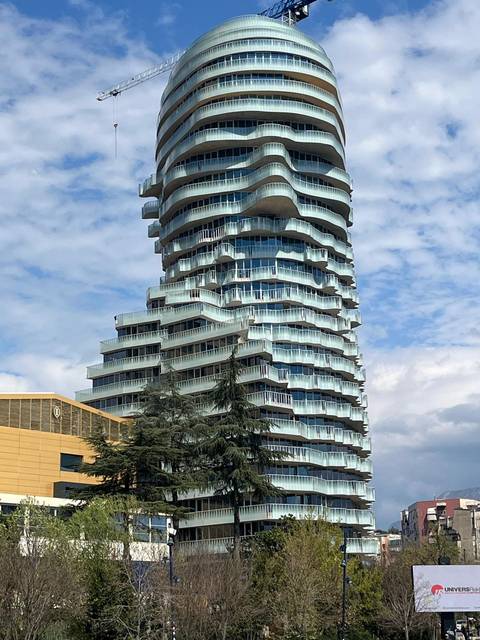 Modern twisting glass skyscraper with wavy balconies rising against partly cloudy sky.