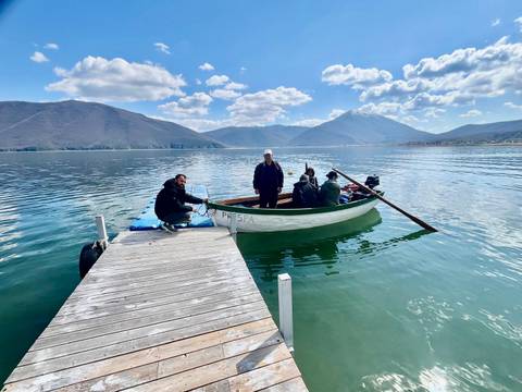 Group boarding a small motorboat from a wooden pier on a mountain lake with snow-capped peaks.