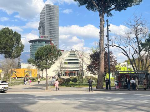 Public square in Tirana with people walking near the renovated Pyramid building and tall tower.